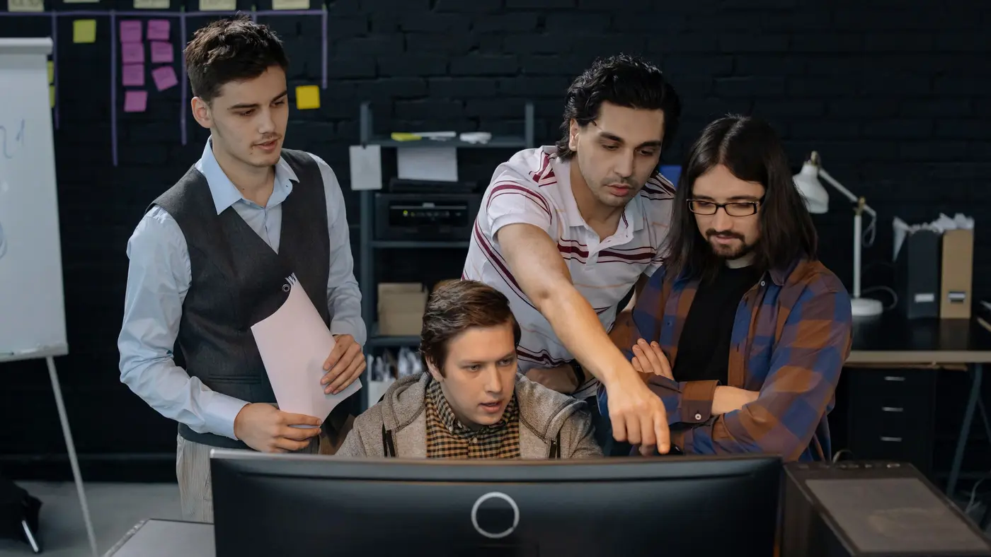 A technology team gathered around a monitor, one pointing at the screen