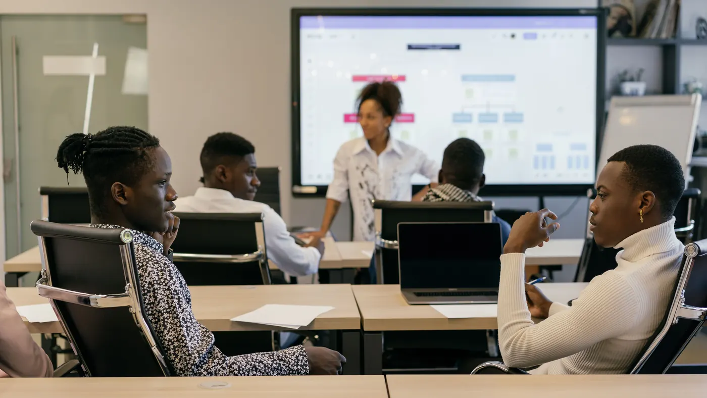 A team in a meeting room reviewing a workflow plan on a digital board shown on a large screen