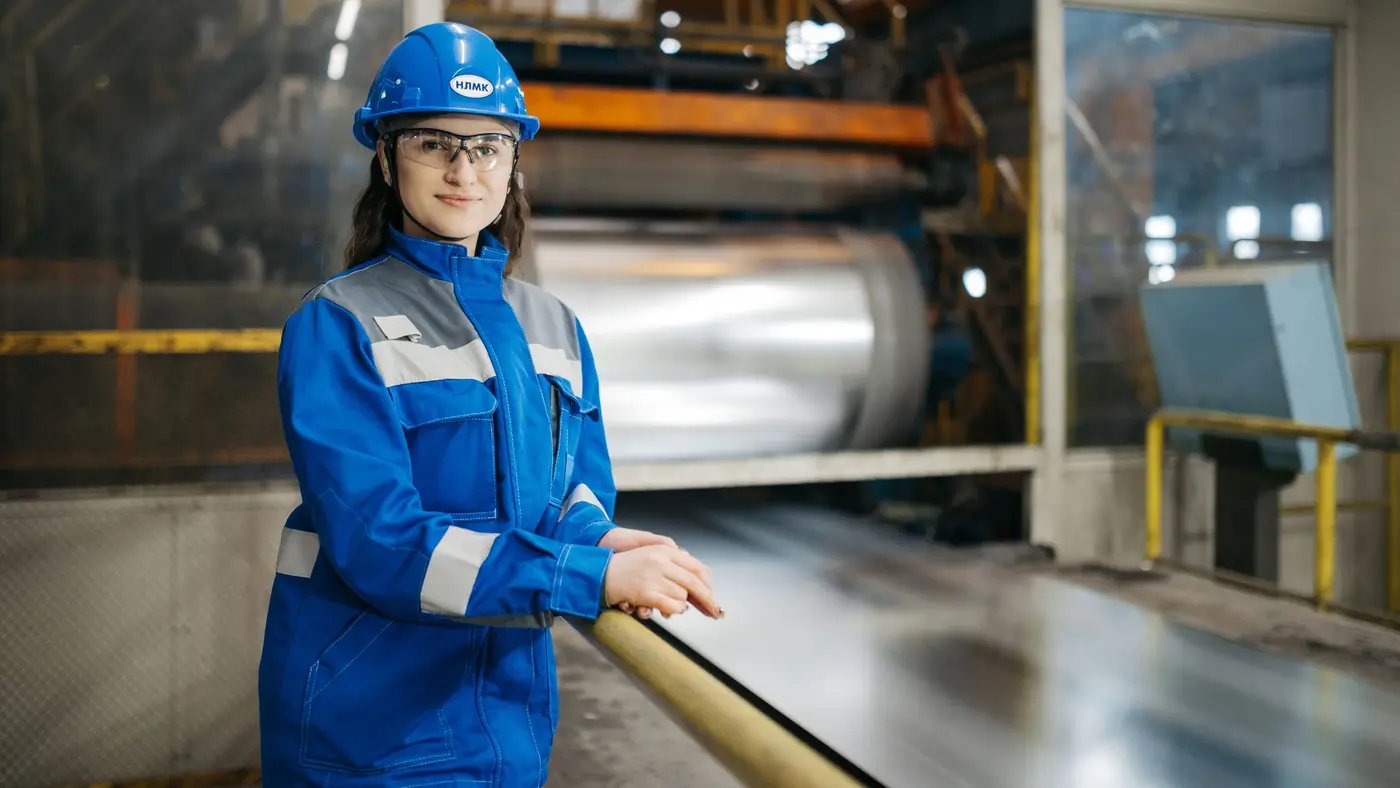 An engineer in a hard hat and blue workwear standing beside production machinery