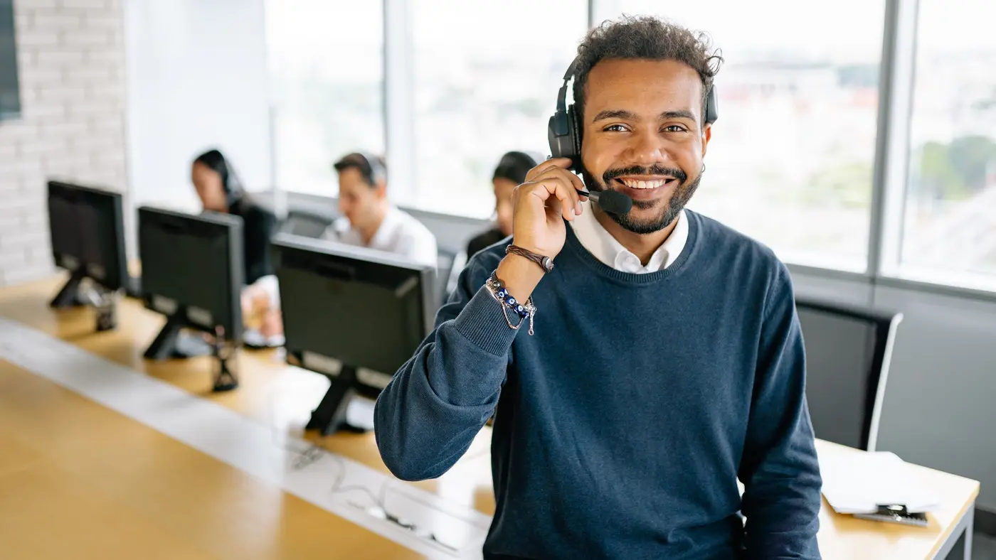 A smiling sales professional wearing a headset in an open office