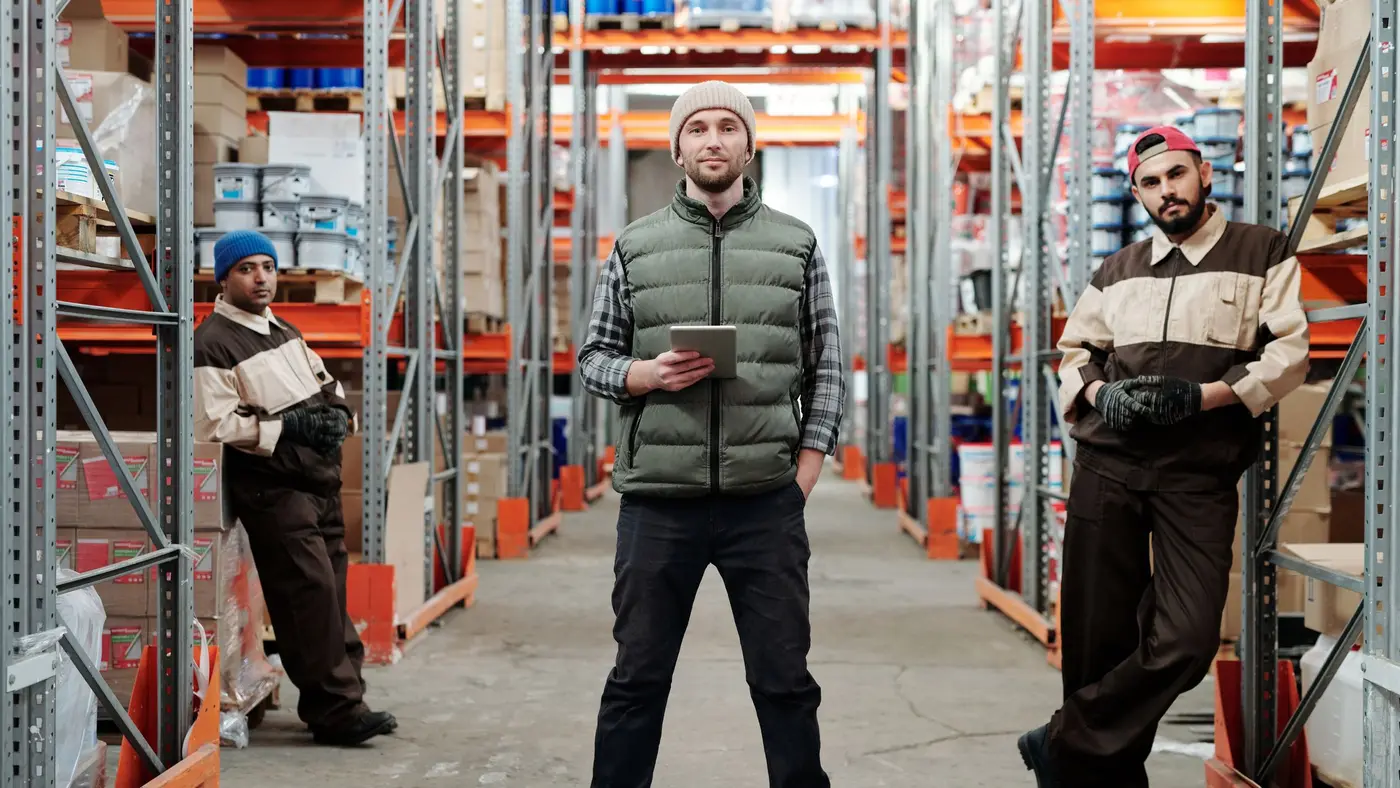 A three-person team standing between stocked shelves in an industrial warehouse